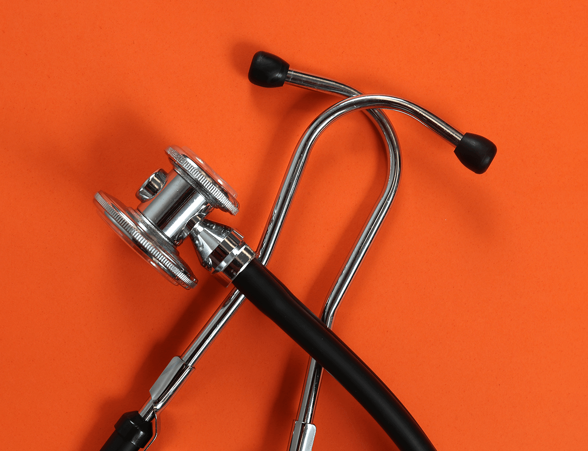 A black stethoscope lying against an orange background.