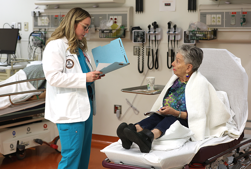 pa-simulation-2026 Physician Assistant student holding a folder speaking with a patient sitting on an examination table in the simulation center.