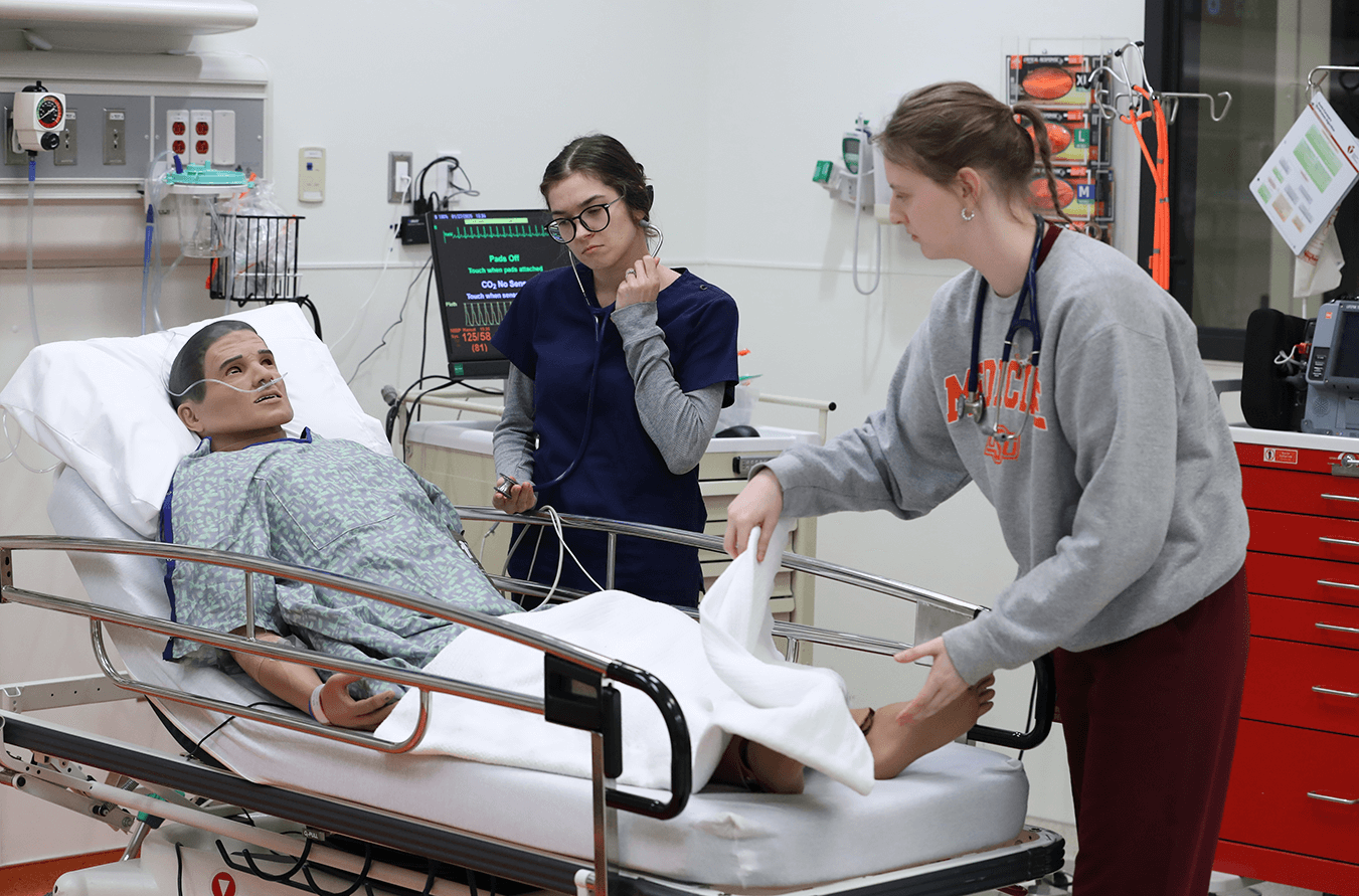 Simulation Club members treat a medical mannequin on a hospital bed.