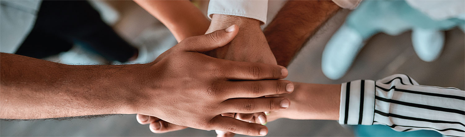 Several people putting their hands on top of one another in the middle of their circle. Several people putting their hands on top of one another in the middle of their circle.
